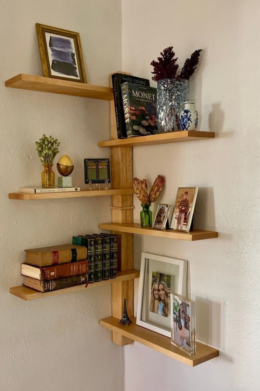 Corner floating shelves with books, framed photos, and decor accents, offering stylish vertical storage for studio apartments in Spring 2025.