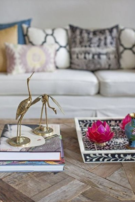 eclectic coffee table decor with stacked books topped with gold bird figurines and a black-and-white floral tray holding colorful lotus candleholders and a small vase

