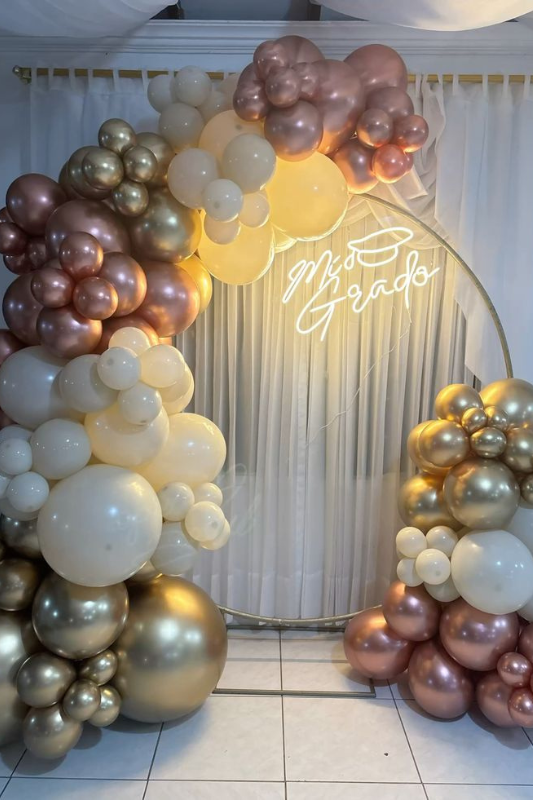 Elegant graduation balloon arch with rose gold, champagne, and ivory balloons framing a "Mi Grado" neon sign, perfect for a chic indoor celebration backdrop. 