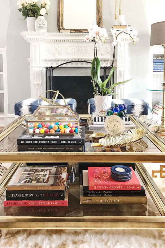 glamorous coffee table styling with stacked design books, orchids in white pots, gold accents, and a clear gumball container for a playful yet elegant living room look

