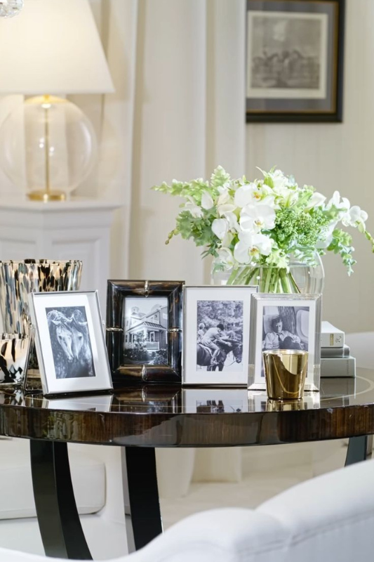 sophisticated living room table styled with black-and-white photo frames, fresh white orchids in a glass vase, and gold accents under a crystal chandelier

