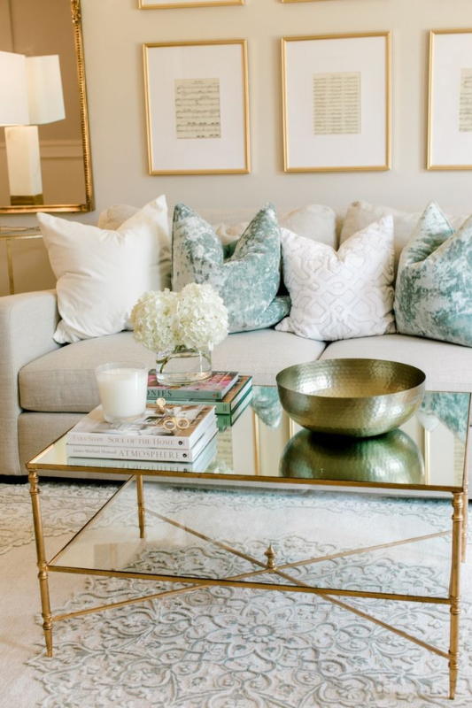 elegant living room with a mirrored glass coffee table styled with white hydrangeas, design books, a candle, and a gold decorative bowl for a luxe touch

