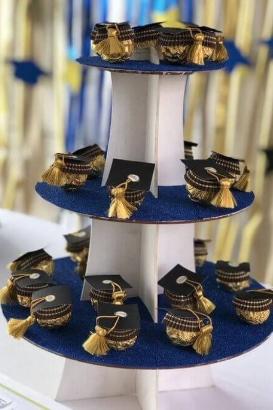 Three-tiered dessert stand with mini graduation cap-themed dessert cups decorated with gold tassels and navy blue accents, displayed at a graduation party.