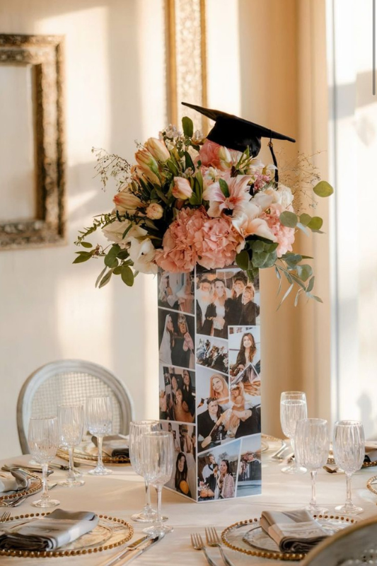 Elegant graduation centerpiece featuring pink and white flowers, a black cap topper, and a custom photo collage on a tall vase — perfect for graduation party table decor.
