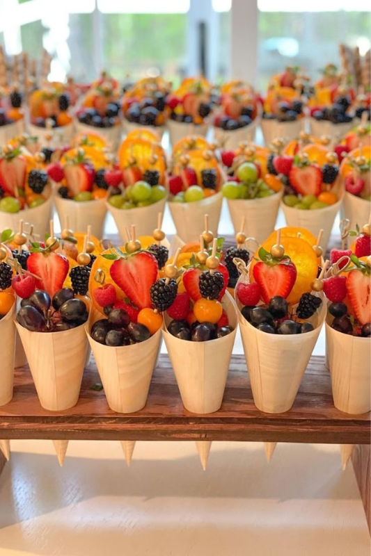 Colorful individual fruit cups in wooden cones served at a graduation party, filled with berries, grapes, and skewers — perfect for a summer celebration or healthy party snack. 