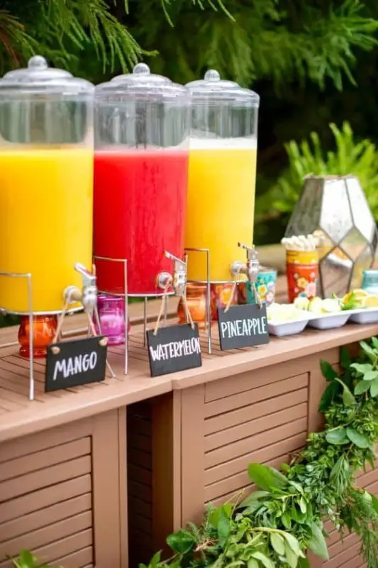 Colorful juice bar station at a graduation party featuring mango, watermelon, and pineapple juices in glass dispensers, perfect for outdoor celebrations and summer events.