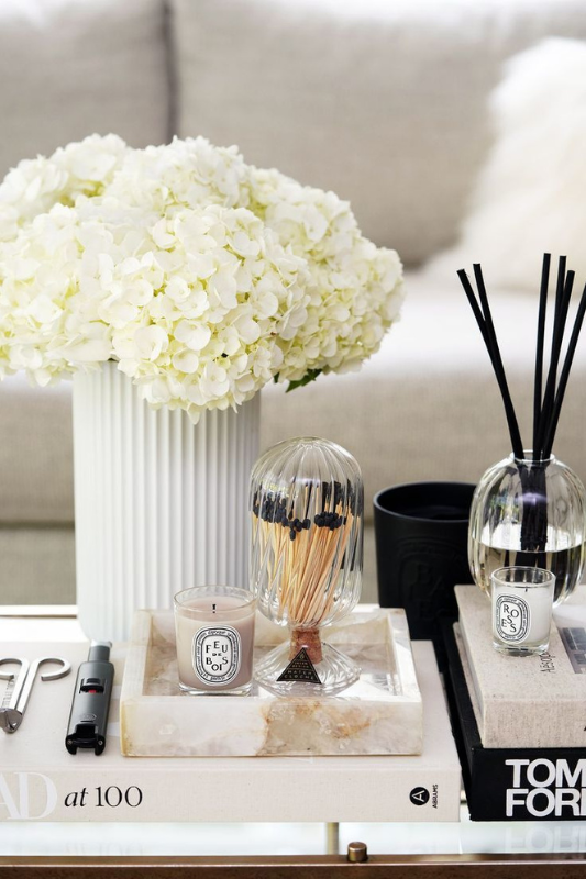 elegant coffee table styling with white hydrangeas in a ribbed vase, designer candles, books, and a glass match cloche for a sophisticated living room look

