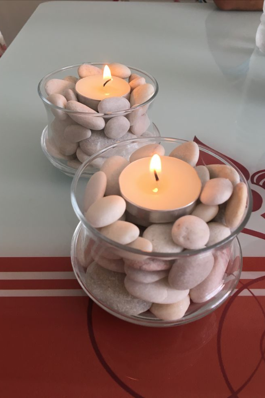 Simple and elegant candle centerpiece featuring tea light candles placed in clear glass votives filled with smooth white and pastel pebbles, styled on a modern tabletop with soft ambient lighting. 