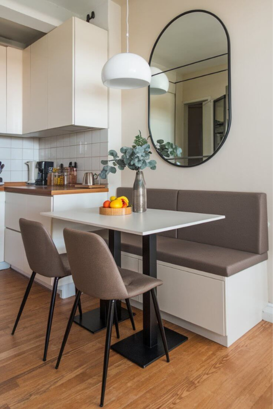Compact kitchen banquette with built-in bench seating, round mirror, and minimalist table perfect for small studio apartment layouts in 2025








