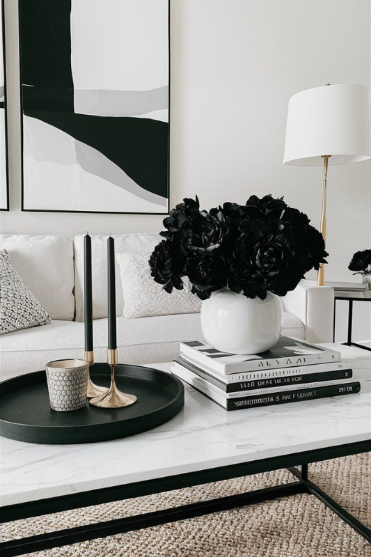 black and white coffee table styling with stacked monochrome books, black faux florals in a white vase, gold candlesticks, and a round black tray in a modern living room


