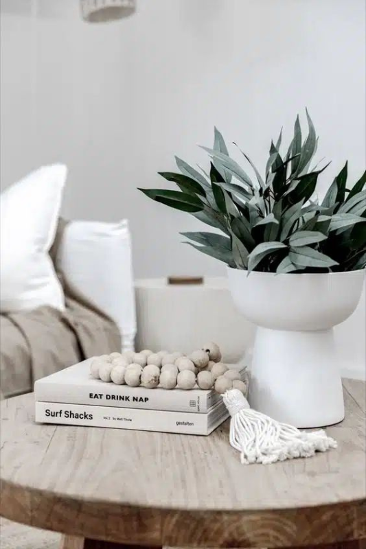 neutral coffee table styling with stacked decor books, wooden beads, and a white planter filled with green foliage in a cozy modern living room

