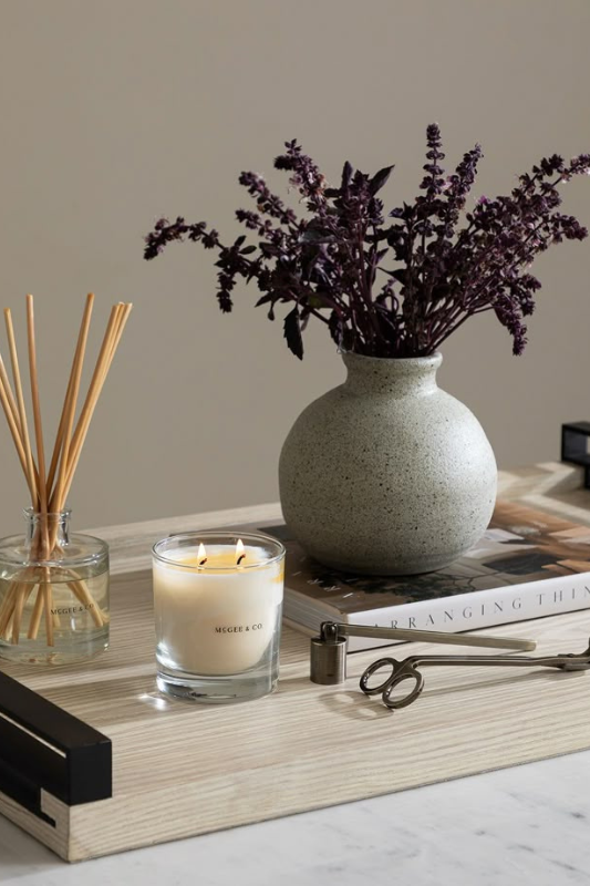 elegant neutral tray styling with McGee & Co. candle, purple foliage in a stone vase, reed diffuser, and decor book on a marble coffee table

