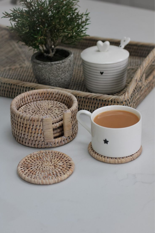 cozy coffee table styling with whitewashed rattan coasters, ceramic cup, striped sugar jar, and mini potted plant on a woven tray

