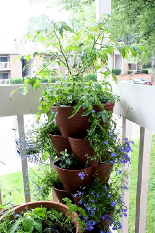 Stacked brown plastic planters filled with trailing blue flowers and herbs, positioned in the corner of a balcony railing to create a vertical garden in a compact space. 