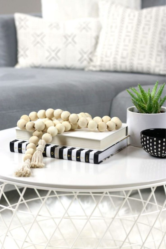 white coffee table styled with striped and neutral books, wood bead garland, potted succulent, and black ceramic bowl in a cozy modern living room

