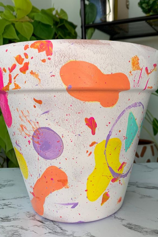 Colorful hand-painted terracotta pot with bold neon splashes and paint splatter in pink, orange, yellow, purple, and teal. This abstract art planter brings energetic, modern style to indoor gardens and creative plant displays.