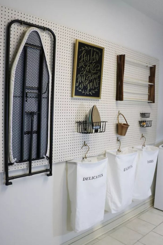 Modern long laundry room with white shaker cabinets, subway tile backsplash, front-loading washer dryer, and black hardware for a clean and functional design
