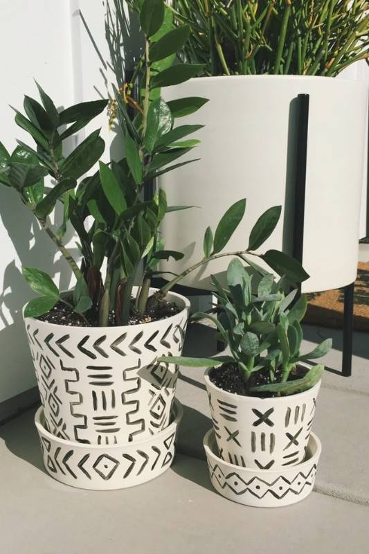 Stylish mudcloth pattern painted terra cotta pots with lush indoor plants displayed on a modern patio. These DIY black and white tribal-inspired planters add a touch of boho decor and natural greenery to small outdoor or apartment balcony spaces.