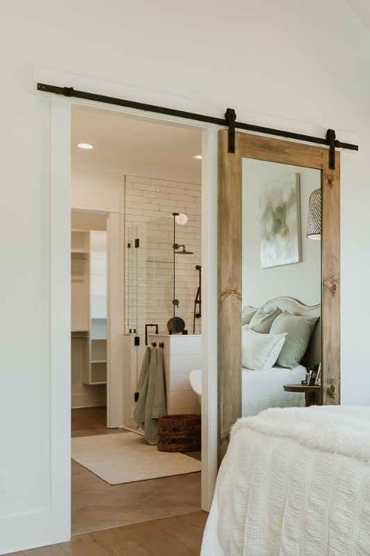 Cozy bedroom view with a rustic wood sliding barn door that includes a full-length mirror, opening into a chic bathroom with subway tiles.