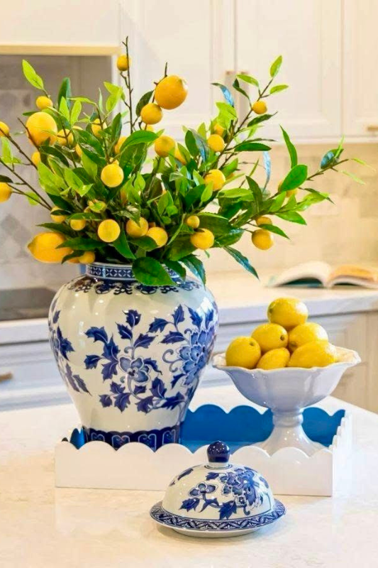 Elegant summer kitchen decor featuring a blue and white ginger jar filled with faux lemon branches, a pedestal bowl of lemons, and matching ceramic dishware on a white tray for a bright seasonal centerpiece 