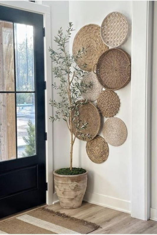 Minimal boho entryway featuring a black front door, neutral rug, potted faux olive tree, and an eye-catching basket wall display with layered natural woven textures for a warm and welcoming look 5/5 