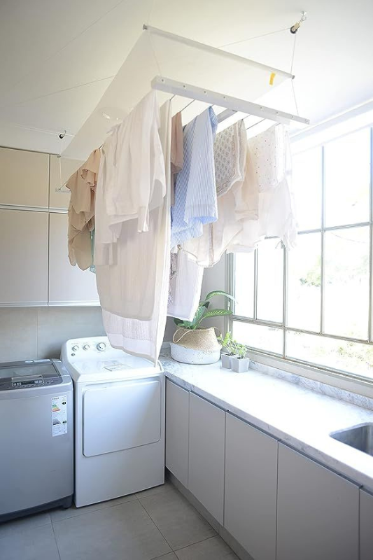 Bright laundry room with ceiling-mounted drying rack, soft white cabinetry, and large windows letting in natural light for an airy feel. 