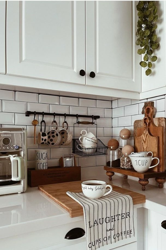 Modern coffee bar setup in a cozy kitchen corner featuring a coffee machine, polka-dot mugs, wall hooks, wooden cutting boards, decorative mugs on risers, and a striped dish towel that reads “Laughter and Cups of Coffee”