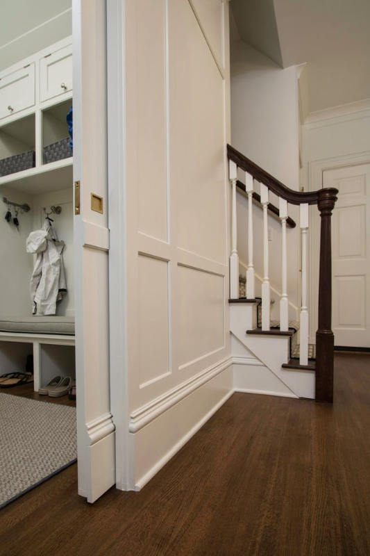 Elegant white pocket door tucked under a traditional staircase, revealing a mudroom with cubby storage and coat hooks.