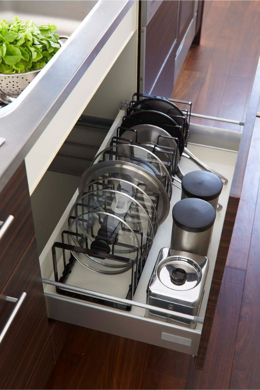 Kitchen drawer organizer with adjustable racks holding stainless steel pot lids and cookware, a smart solution for deep drawer organization and maximizing lower cabinet space. 