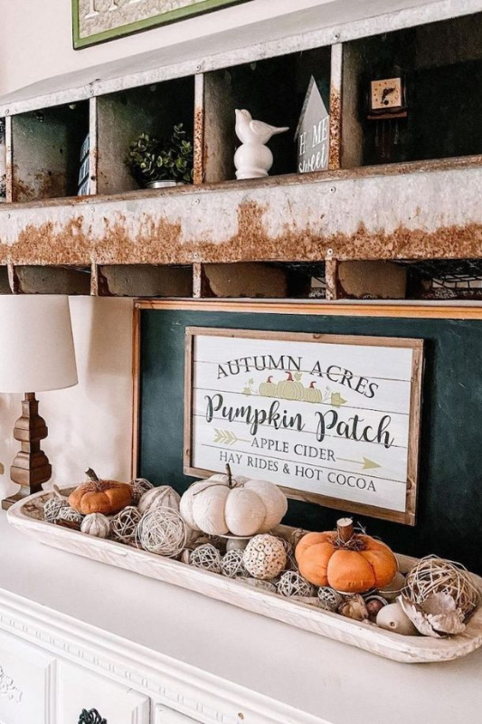 Farmhouse-style fall dough bowl centerpiece displayed on a white dresser, featuring neutral and orange pumpkins, rattan balls, and decorative fillers beneath a rustic "Pumpkin Patch" autumn sign.