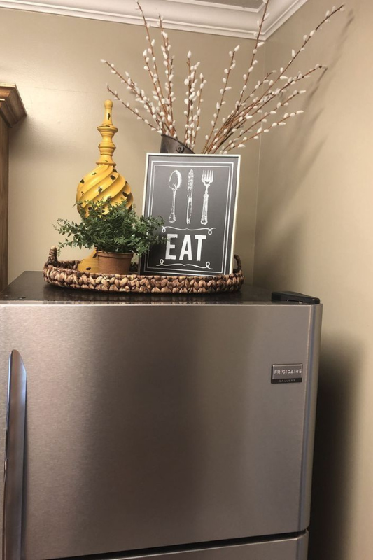 Farmhouse-style fridge top decor with framed “EAT” sign, faux greenery, and rustic tray for cozy kitchen styling