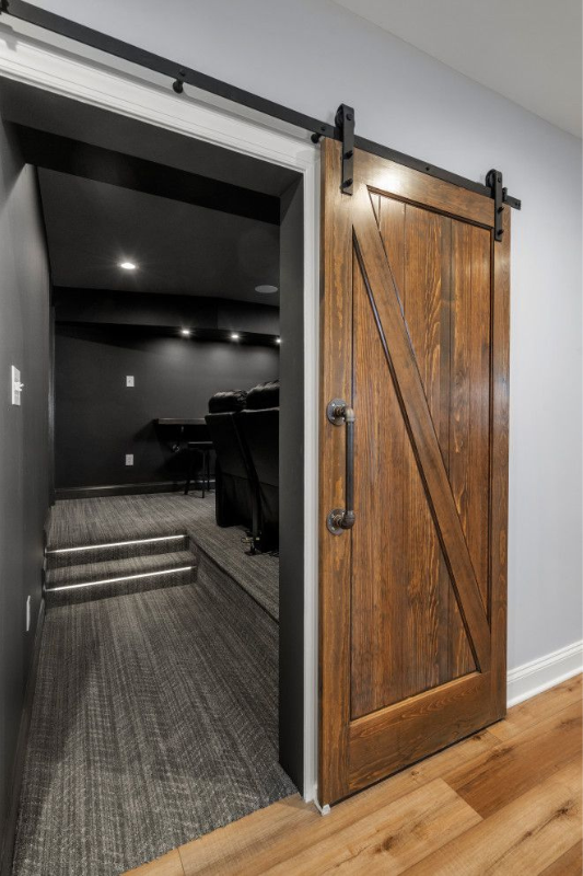 Stylish home theater entry with black walls, cozy carpeted flooring, and a rustic wood sliding barn door for a dramatic yet welcoming look.
