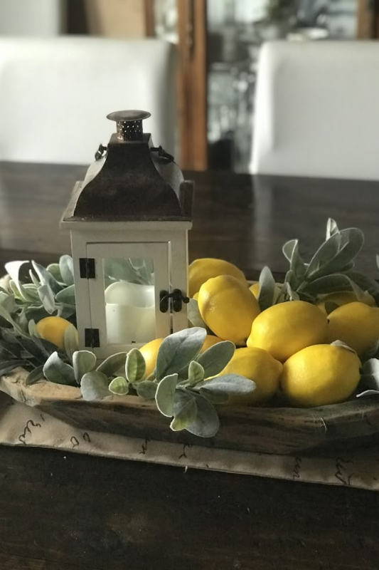 Farmhouse dough bowl centerpiece with faux lemons, soft greenery, and a rustic white lantern on a dark wood dining table for spring or summer decor