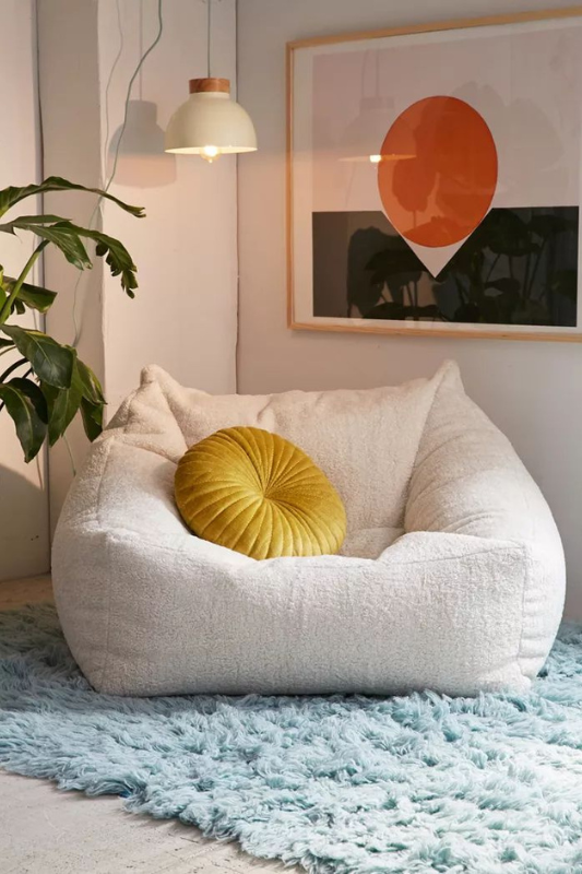 Cozy living room corner with boucle beanbag chair, yellow velvet pillow, shaggy aqua rug, modern wall art, and pendant light