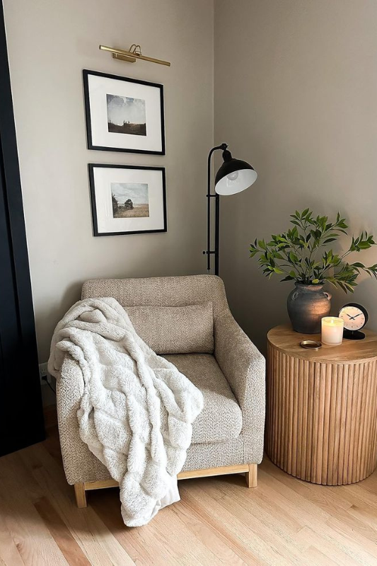 Neutral living room corner with boucle armchair, faux fur throw, fluted wood side table, black floor lamp, and framed wall art