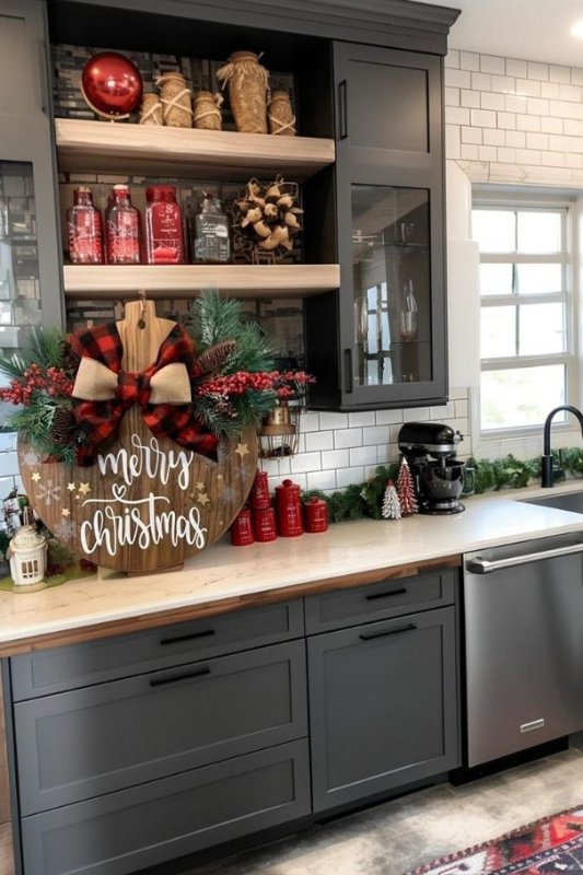 Festive Christmas kitchen decor featuring a wooden “Merry Christmas” sign with pine accents, red holiday jars, and dark gray shaker cabinets, styled with modern farmhouse charm and seasonal warmth. 
