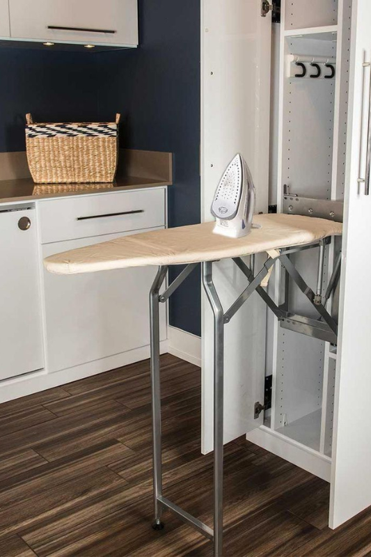 Compact modern laundry room with stacked Bosch washer and dryer, sage green cabinetry, brass faucet, and under-shelf task lighting for efficient small space design.
