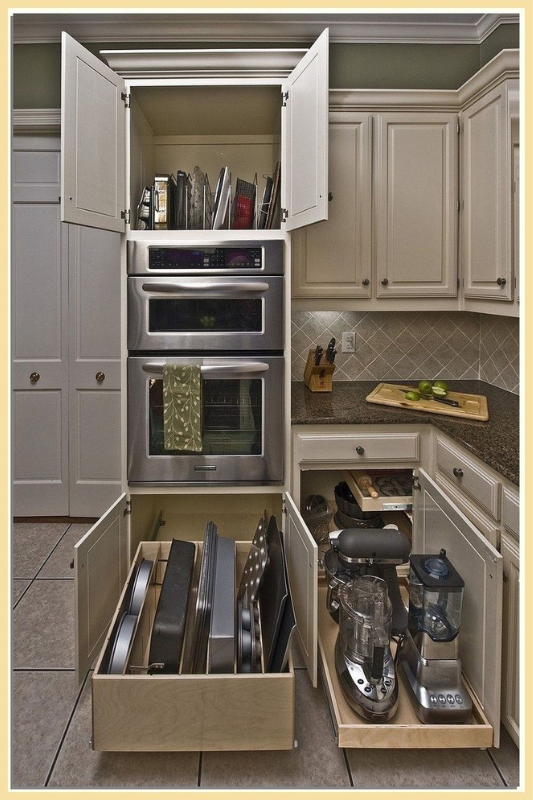 Pull-out cabinet drawers storing baking sheets and small appliances like blenders and food processors, providing practical vertical storage solutions in a modern kitchen layout. 