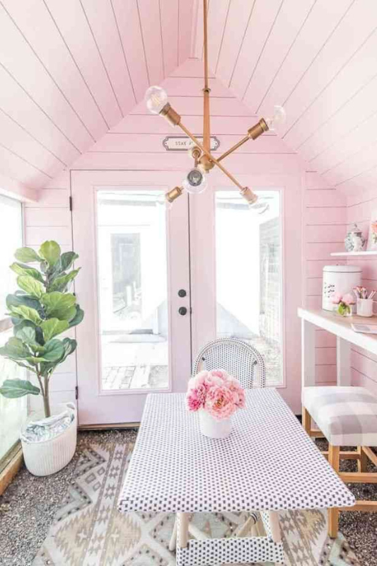 Bright she shed painted in soft pink with a gold modern chandelier, polka dot table, and natural light.