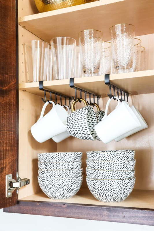 Creative cabinet organization using under-shelf mug hooks, with hanging cups and neatly stacked patterned bowls, maximizing vertical space in a compact kitchen cabinet setup. 