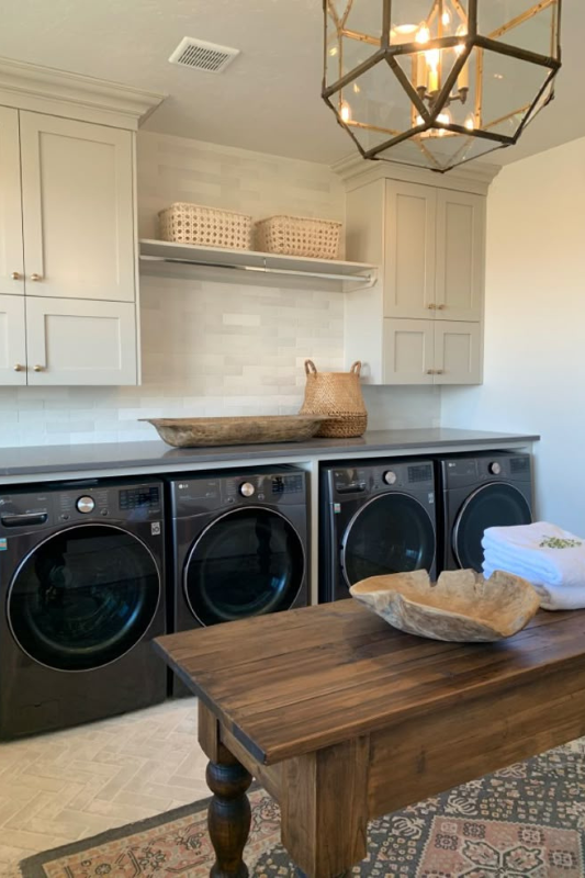Vintage white laundry room with Samsung washer and dryer, farmhouse sink, patterned black and white tile flooring, and woven storage baskets. 