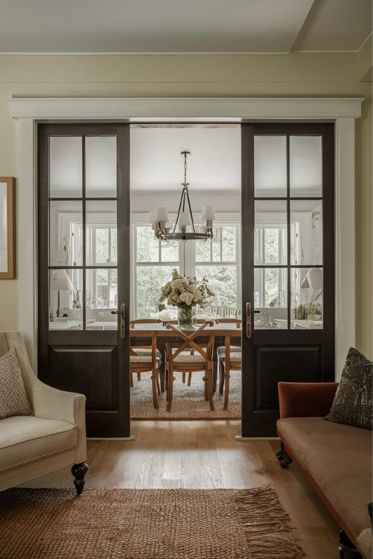 White sliding French doors separating a cozy bedroom from a living area with modern decor and wooden flooring.