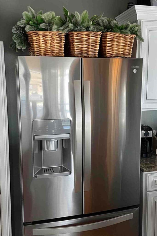 Wicker baskets with faux greenery arranged on top of a stainless steel fridge for warm farmhouse-style kitchen decor