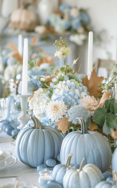 Soft blue pumpkins, white taper candles, hydrangea floral centerpiece, and mixed autumn leaves for a romantic fall table.